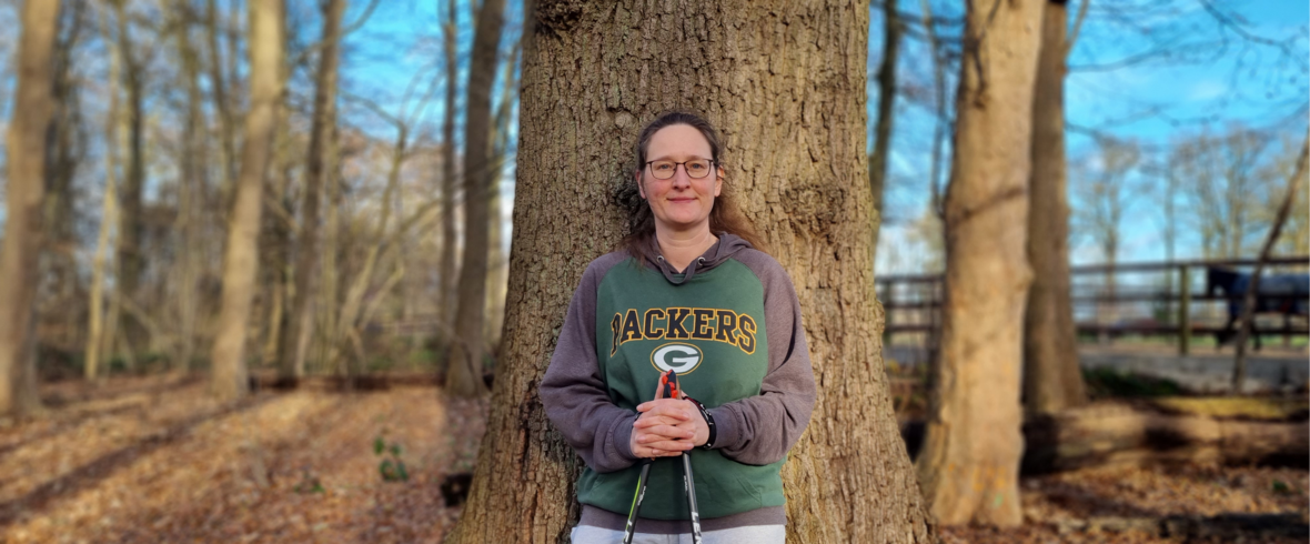 Eine Frau lehnt an einem Baum und lächelt in die Kamera